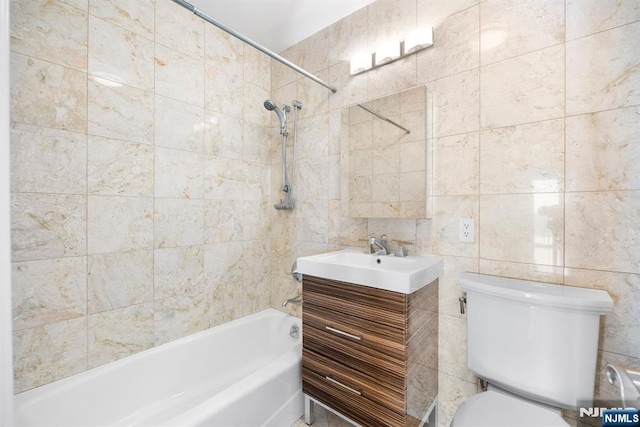 full bathroom with vanity, toilet, tiled shower / bath combo, and tile walls