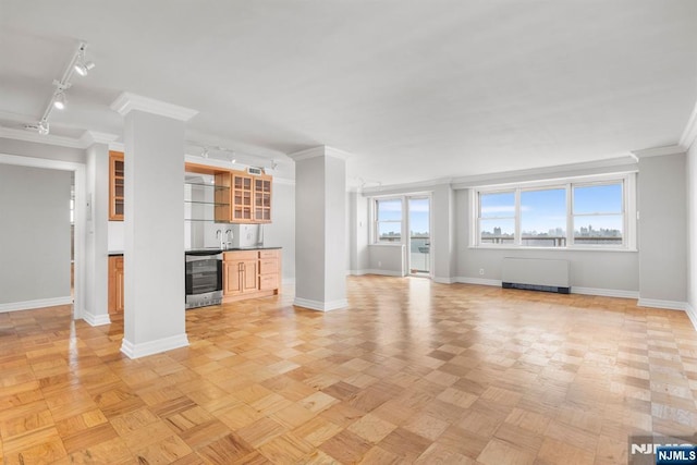 unfurnished living room featuring rail lighting, ornamental molding, radiator, light parquet flooring, and beverage cooler