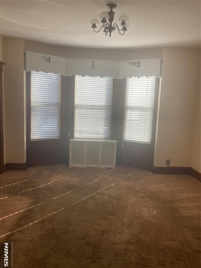 unfurnished room featuring radiator, a chandelier, and dark carpet