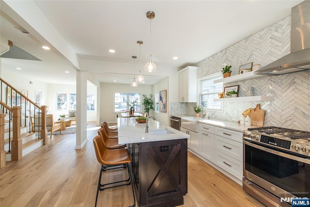 kitchen with white cabinetry, sink, light stone counters, gas range, and wall chimney range hood