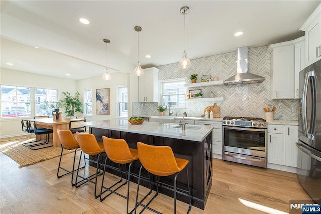 kitchen featuring white cabinetry, wall chimney range hood, hanging light fixtures, and appliances with stainless steel finishes