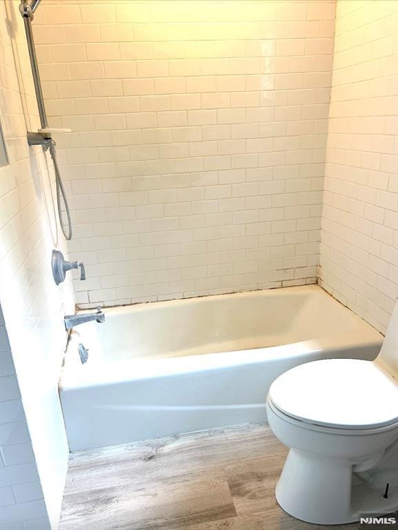 bathroom with tiled shower / bath combo, wood-type flooring, and toilet