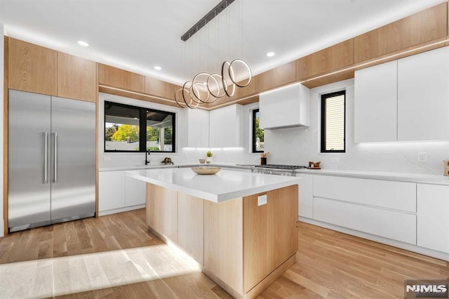 kitchen with white cabinetry, built in refrigerator, decorative light fixtures, a kitchen island, and wall chimney range hood