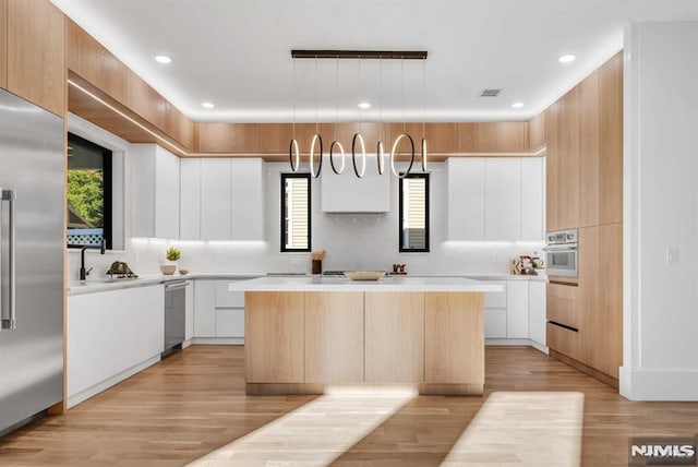 kitchen featuring appliances with stainless steel finishes, a center island, white cabinets, decorative light fixtures, and light wood-type flooring