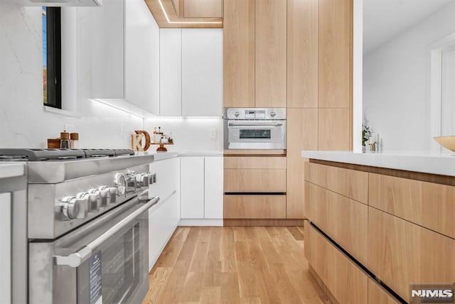 kitchen featuring white cabinetry, appliances with stainless steel finishes, light brown cabinets, and light wood-type flooring