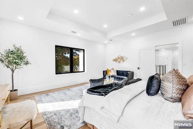 bedroom with a tray ceiling and light hardwood / wood-style floors