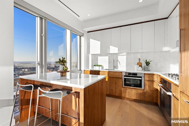 kitchen with sink, light hardwood / wood-style flooring, white cabinetry, stainless steel appliances, and a kitchen breakfast bar