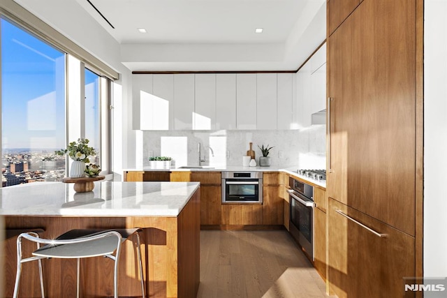 kitchen featuring sink, light hardwood / wood-style flooring, backsplash, a kitchen breakfast bar, and stainless steel appliances