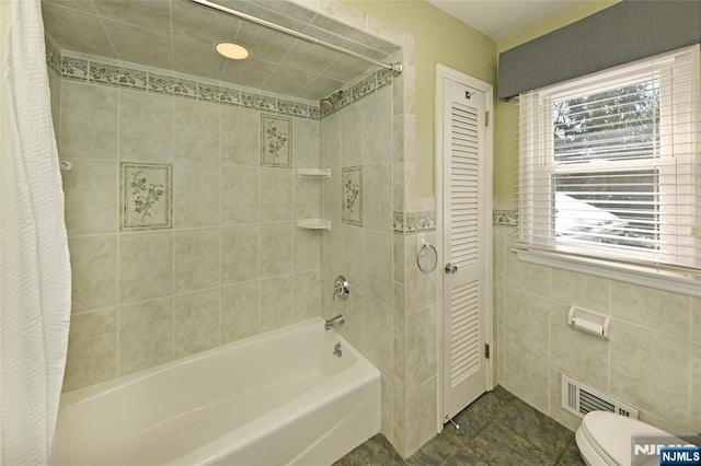 bathroom featuring shower / bath combination with curtain, tile patterned floors, toilet, and tile walls