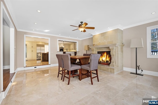 dining room featuring a tiled fireplace, ornamental molding, and ceiling fan