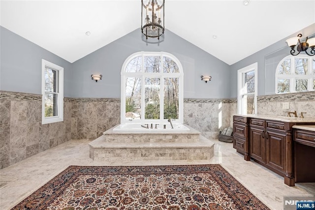 bathroom with tiled tub, vaulted ceiling, plenty of natural light, and an inviting chandelier