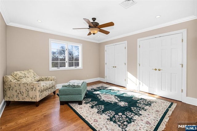 living area with crown molding, wood-type flooring, and ceiling fan