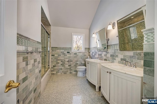 full bathroom with toilet, vaulted ceiling, tile walls, vanity, and enclosed tub / shower combo