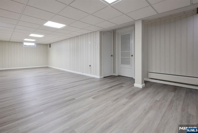 basement featuring a drop ceiling, baseboard heating, and light wood-type flooring