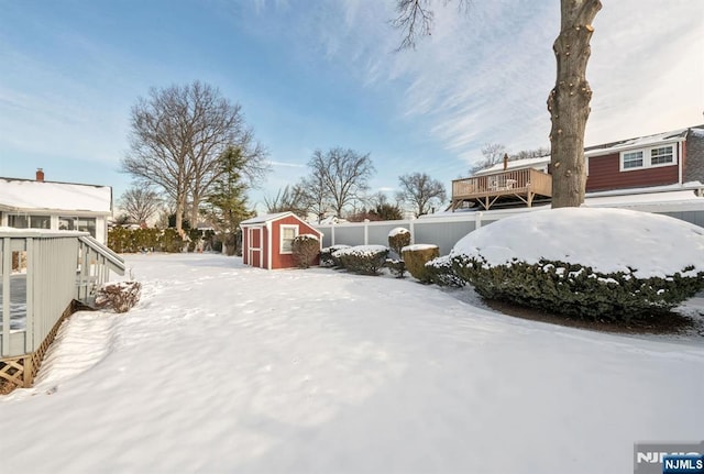 snowy yard with a storage shed and a wooden deck