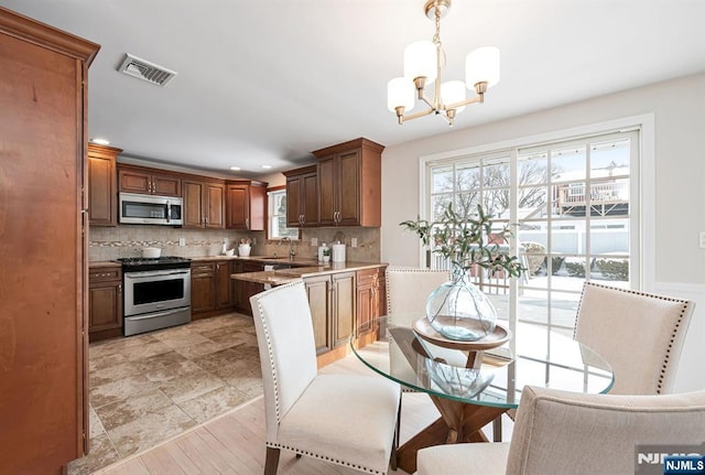 kitchen with sink, tasteful backsplash, an inviting chandelier, decorative light fixtures, and stainless steel appliances