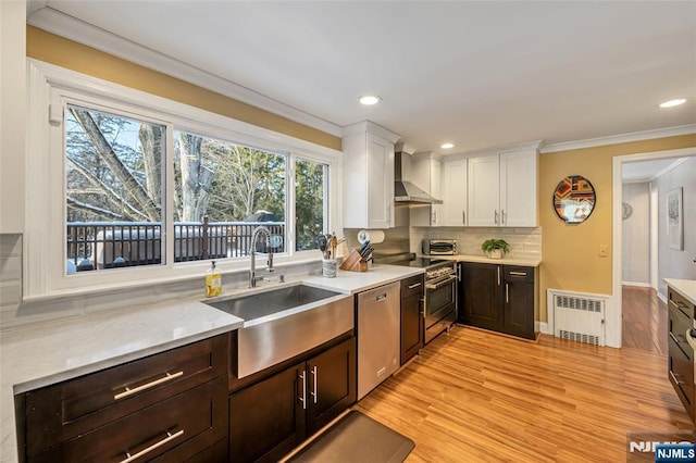 kitchen with wall chimney exhaust hood, sink, white cabinetry, radiator, and stainless steel appliances