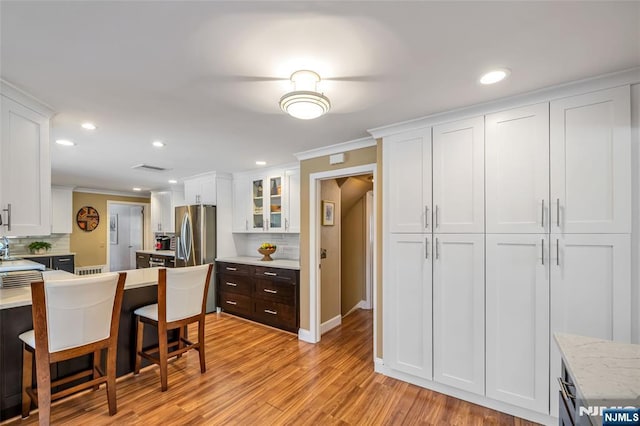 kitchen with light hardwood / wood-style flooring, a breakfast bar, white cabinetry, ornamental molding, and decorative backsplash