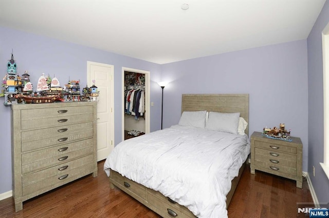 bedroom with a spacious closet, dark wood-type flooring, and a closet