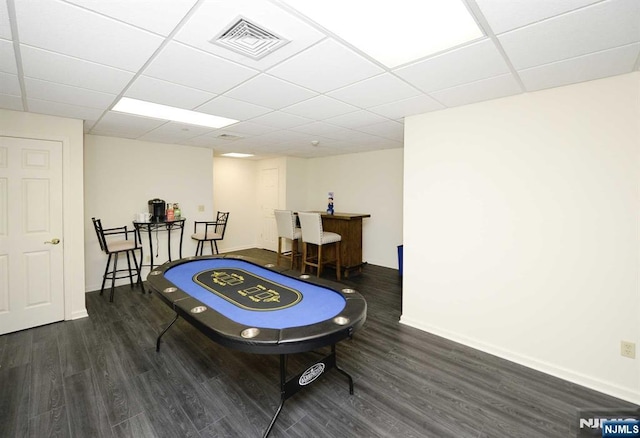 game room with dark hardwood / wood-style flooring, bar, and a drop ceiling