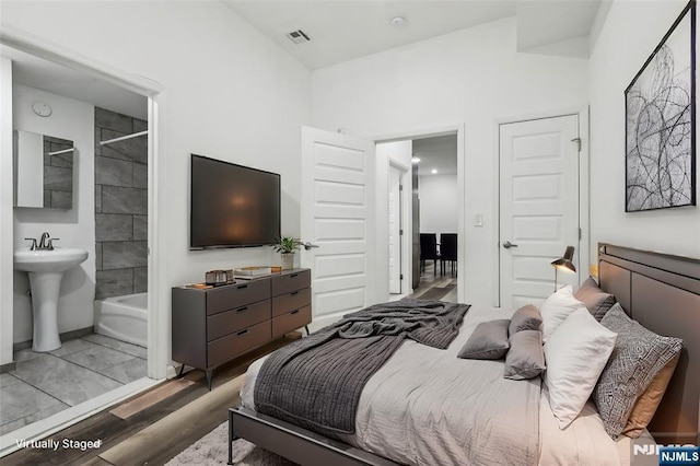 bedroom with visible vents, a sink, ensuite bath, and wood finished floors