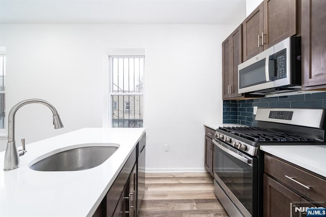 kitchen with a sink, dark brown cabinetry, light countertops, appliances with stainless steel finishes, and tasteful backsplash