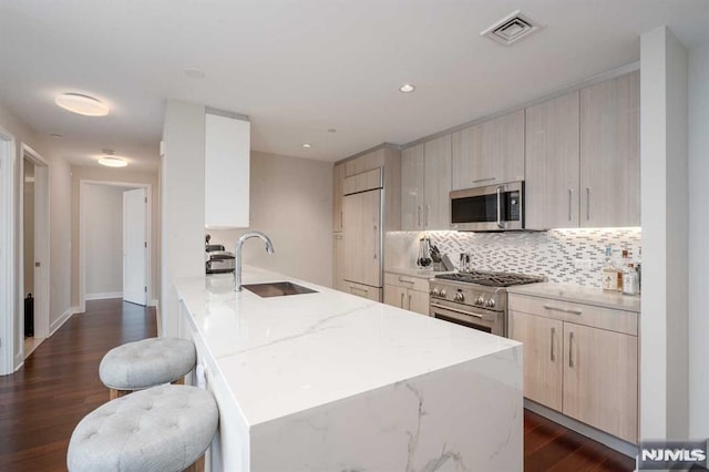 kitchen with sink, a breakfast bar, dark hardwood / wood-style floors, premium appliances, and light stone countertops