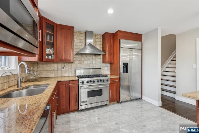 kitchen with high quality appliances, sink, decorative backsplash, light stone counters, and wall chimney exhaust hood