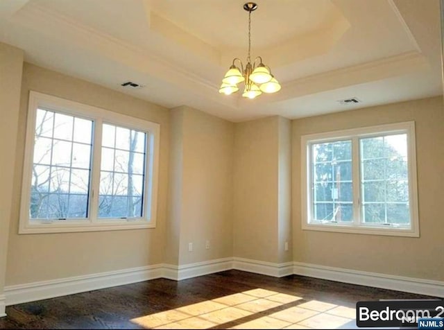 spare room featuring a chandelier, wood finished floors, a raised ceiling, and visible vents