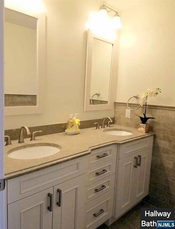 bathroom with a wainscoted wall, double vanity, a sink, and tile walls