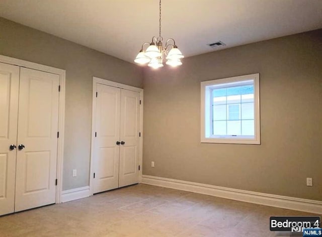 unfurnished bedroom with a notable chandelier, baseboards, visible vents, and multiple closets