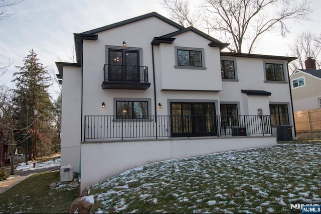 snow covered house with fence, a balcony, and stucco siding