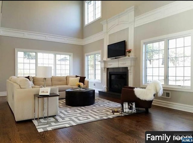 living room featuring visible vents, baseboards, a glass covered fireplace, dark wood-style flooring, and a high ceiling