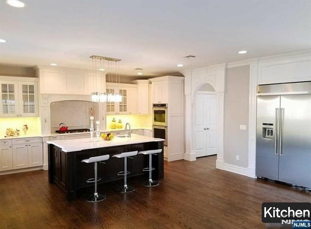 kitchen with a center island with sink, dark wood finished floors, appliances with stainless steel finishes, light countertops, and a sink