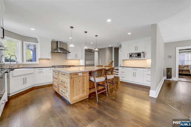 kitchen featuring wall chimney range hood, decorative backsplash, hanging light fixtures, and a kitchen island