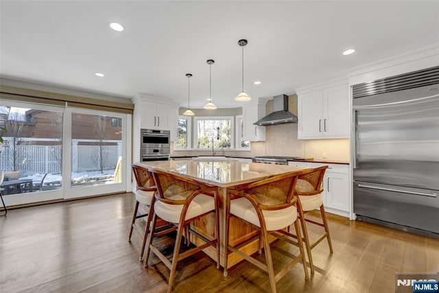 kitchen with wall chimney exhaust hood, stainless steel appliances, hanging light fixtures, and white cabinets