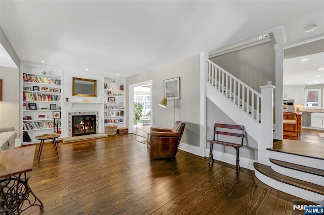 living room with built in shelves, a high end fireplace, and dark hardwood / wood-style floors