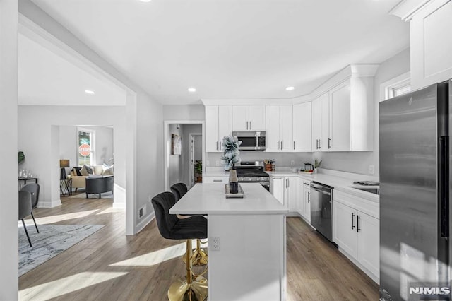 kitchen featuring white cabinetry, a kitchen island, stainless steel appliances, a kitchen bar, and light wood-type flooring