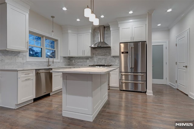 kitchen featuring wall chimney exhaust hood, decorative light fixtures, appliances with stainless steel finishes, a kitchen island, and white cabinets