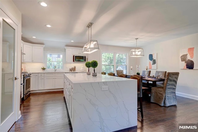 kitchen featuring white cabinetry, tasteful backsplash, decorative light fixtures, a center island, and appliances with stainless steel finishes