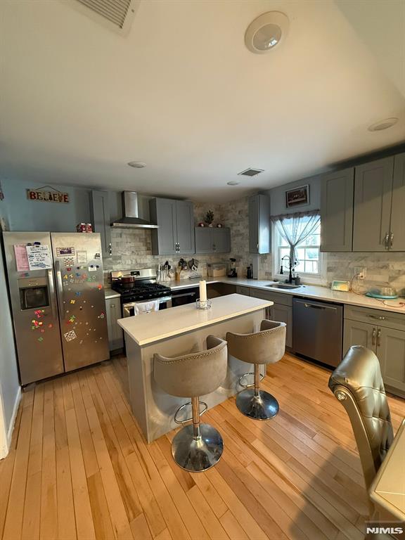 kitchen with wall chimney exhaust hood, sink, light wood-type flooring, a kitchen island, and stainless steel appliances