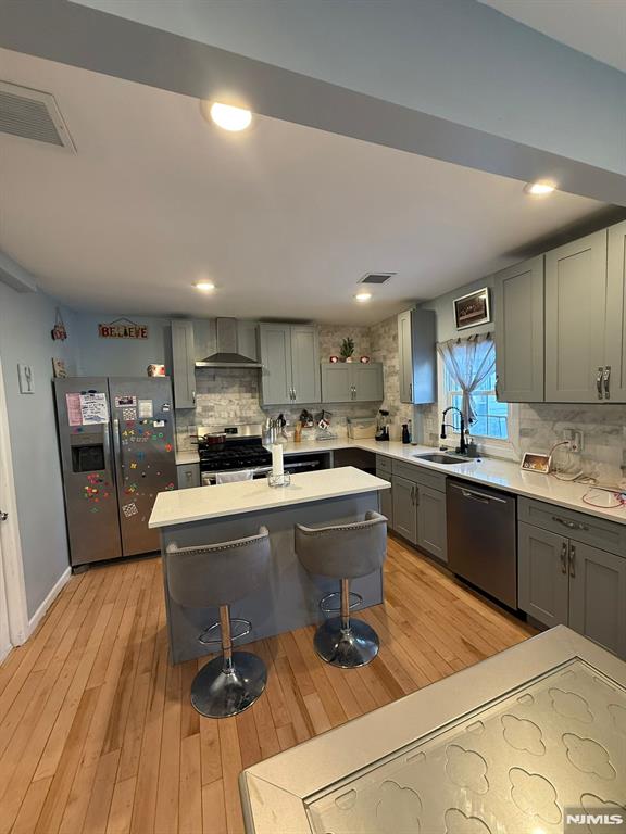 kitchen with sink, a center island, appliances with stainless steel finishes, a kitchen breakfast bar, and wall chimney range hood