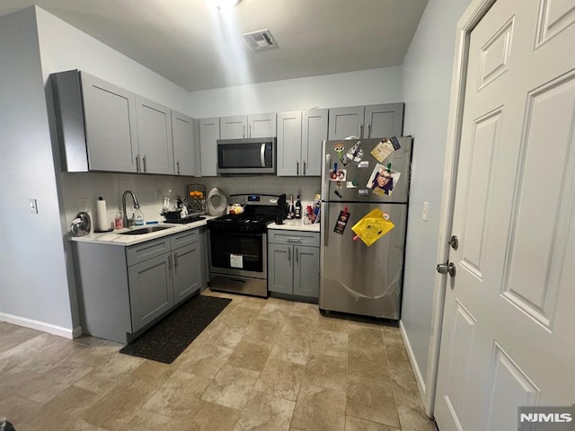 kitchen featuring tasteful backsplash, stainless steel appliances, sink, and gray cabinetry