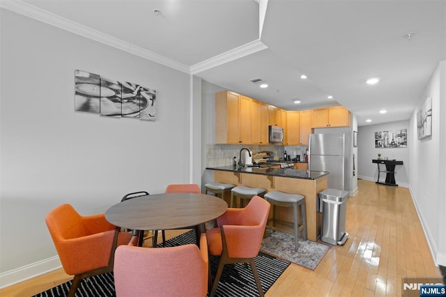 kitchen with crown molding, light brown cabinets, appliances with stainless steel finishes, kitchen peninsula, and backsplash