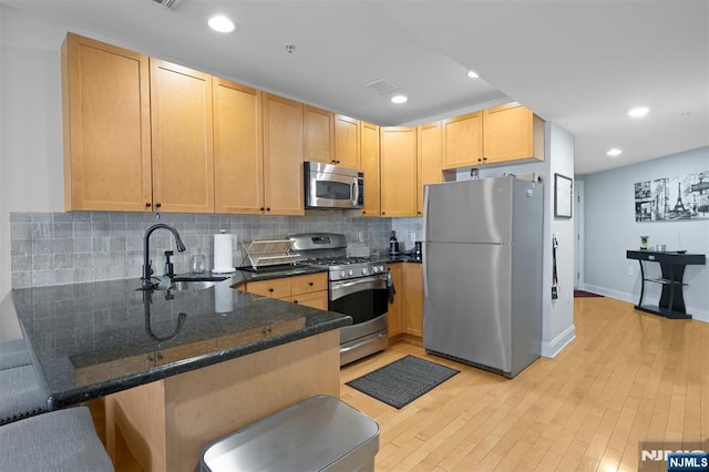 kitchen with appliances with stainless steel finishes, light brown cabinetry, sink, dark stone countertops, and kitchen peninsula