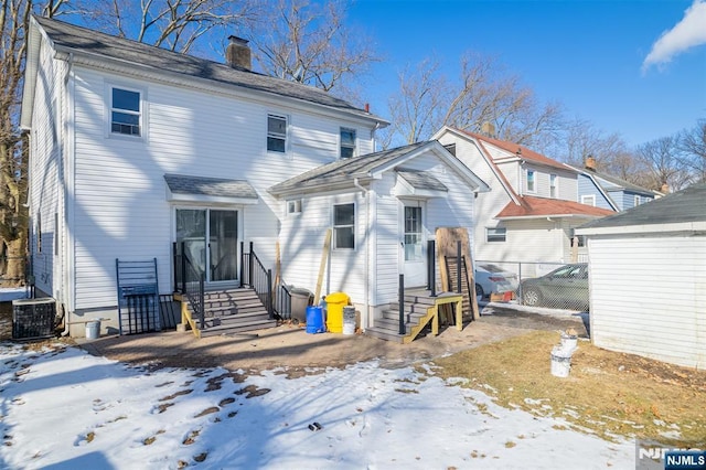 snow covered back of property with entry steps, a chimney, fence, and cooling unit