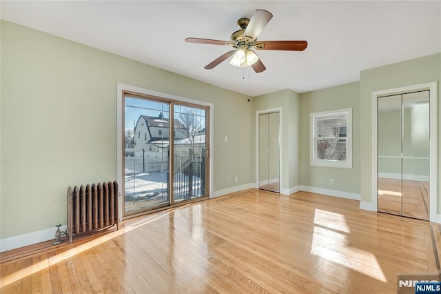 unfurnished room with light wood-style floors, radiator heating unit, baseboards, and a ceiling fan