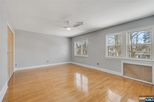 spare room with ceiling fan, radiator heating unit, light wood-style flooring, and baseboards