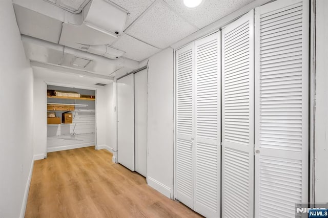 corridor featuring light wood-type flooring and a drop ceiling