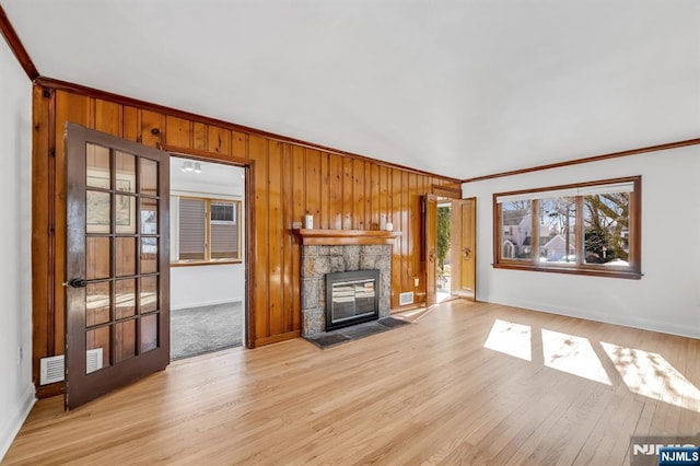 unfurnished living room featuring light hardwood / wood-style flooring, a stone fireplace, crown molding, and wooden walls